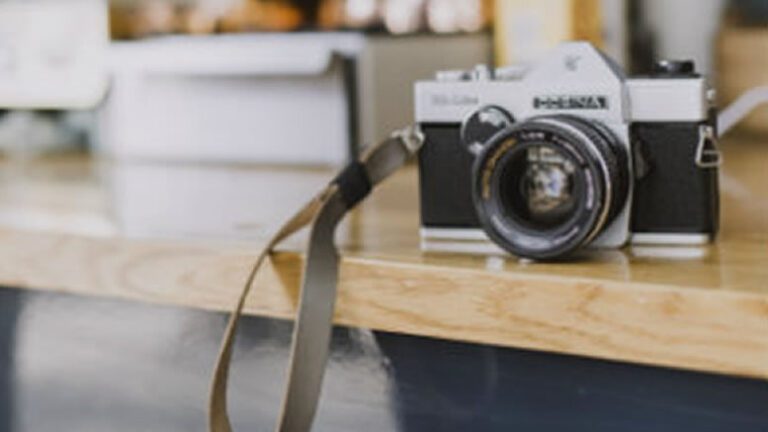 A vintage camera with a strap on a wooden table.