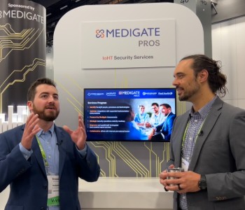Two men discussing at a Medigate PROS booth in a professional setting.
